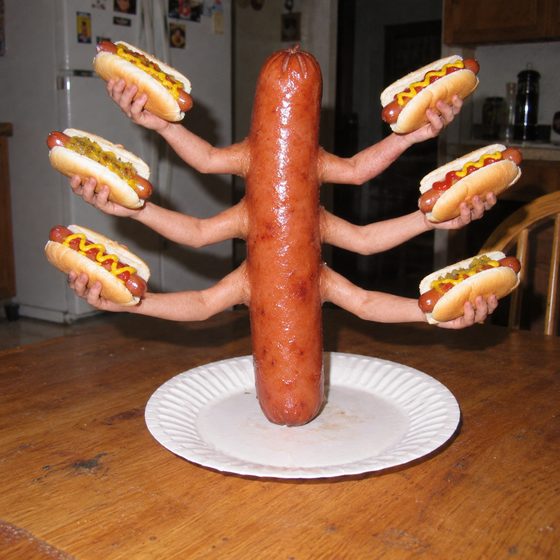 A hot dog with eight human arms holding hot dogs