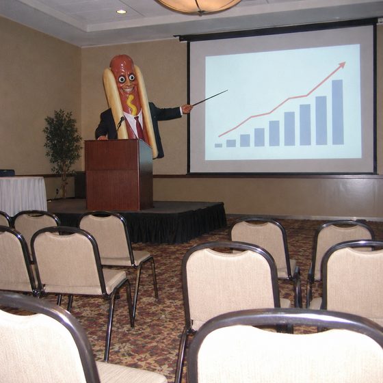 A hot dog in a suit presenting to an empty conference room